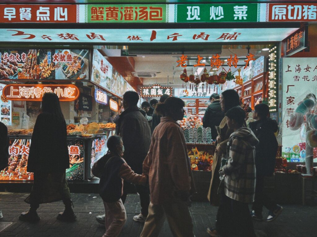 Shoppers walking past brightly lit snack shops on a Shanghai street at night