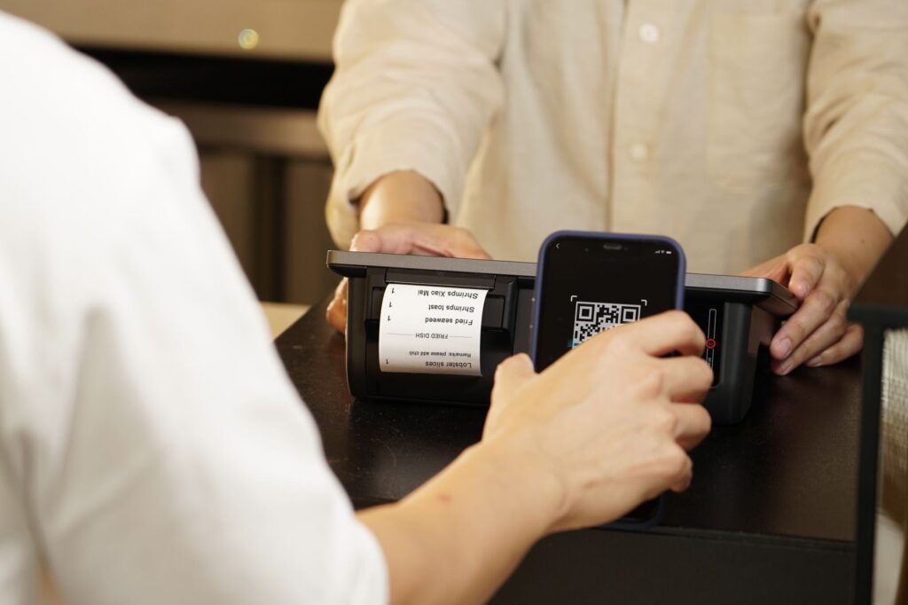 Customer showing a payment QR code on their phone to a cashier’s scanner at a shop counter